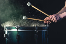 A Man Plays A Musical Percussion Instrument With Sticks On A Dark Background.