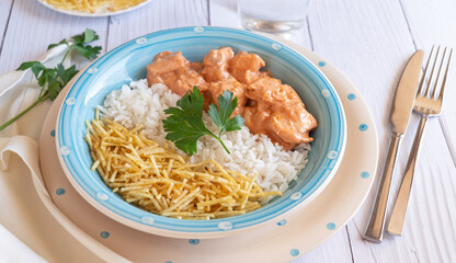 Wall Mural - Close-up of Chicken strogonoff with rice and potato straw on white wooden table. Brazilian cuisine.