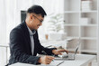 © Kritdanai - Happy working asian businessman talking on the phone with accounting documents at desk in happy working office