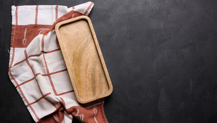 Wooden board and folded linen linen kitchen towel on a black background, top view. Copy space
