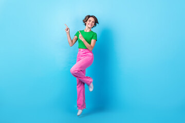 Full length photo of pretty sweet lady wear green t-shirt showing two fingers empty space jumping high isolated blue color background