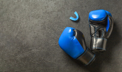 Boxing gloves of blue color with a mouthguard on a black background. Free space for text