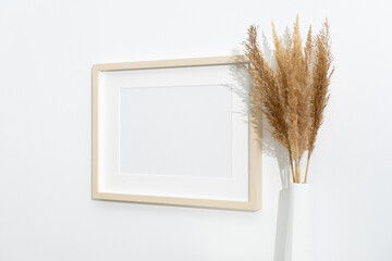 Wooden artwork frame mockup on white wall with dry grass decoration, blank mockup with copy space