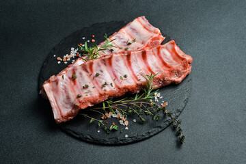 Wall Mural - Fresh raw ribs with rosemary, spices and herbs. On a dark slate background. Top view. Free space for text.