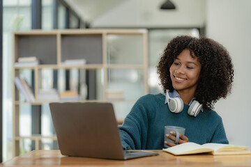 Young female student wearing headphones studying online training video communication Happy female student looking at computer screen, watching webinars or making video chat on webcam in library.