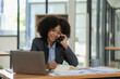 © ArLawKa - Smiling african-american female accountant talking on the phone using laptop sitting at her office Internet technology. mobile communication online in office business concept