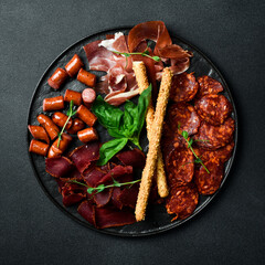 Wall Mural - Antipasto plate: prosciutto, salami, pepperoni and grissini. On a dark background, close-up.