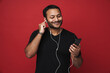 © Drobot Dean - Indian man listening music with earphones and mobile phone isolated over red wall