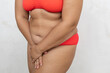 Unrecognizable overweight, fat, adipose woman in red lingerie holding thighs and bikini zone after epilation on white studio background. Hair removing for sensitive skin. Lazer, wax and razor methods
