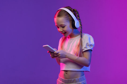 Wall Mural - Pretty preteen blonde girl using smartphone and headphones, copy space