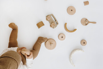 Top view of cute one year old baby in brown hat plays with stylish wooden toys. Minimal baby fashion online shop, online store concept