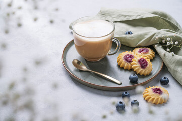 Wall Mural - Cappuccino or latte with milk foam in a cup with homemade berry cookies and blueberries on a light background with gypsophila branches. Concept spring morning breakfast.