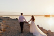 Wedding couple holds each other hands while walking on the beach against the sunset. Outdoor wedding ceremony on the seashore.