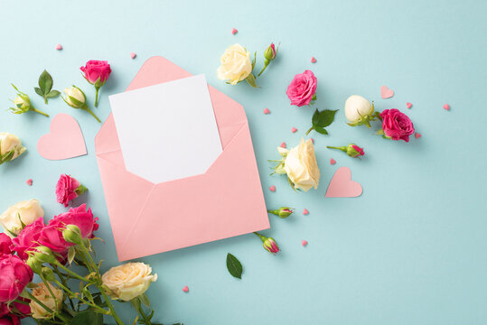 Mother's Day concept. Top view of an open pink envelope with blank space for copy or greeting with stunning rose flowers on a pastel blue background