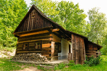 Beautiful Wooden Old House In Green Forest With Pile Of Wood Stored In Front, Ready For Winter.