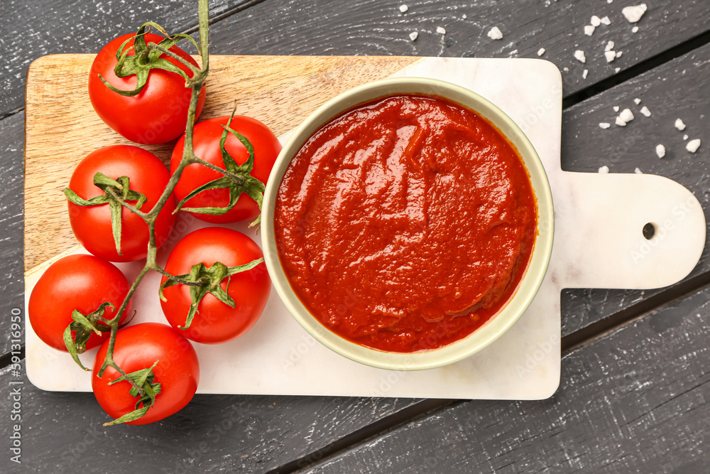 Bowl with tasty tomato paste and fresh vegetables on dark wooden background