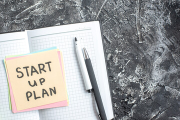 Wall Mural - top view start up plan note on sticker inside open copybook on gray background lesson student notepa