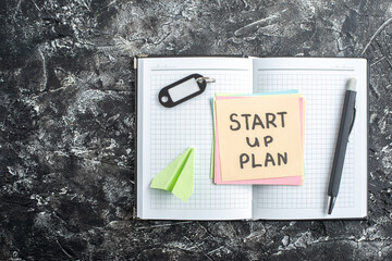 Wall Mural - top view start up plan note on sticker inside open copybook on gray background lesson student notepa