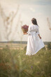 © junky_jess - Beautiful woman in vintage white dress with a wicker basket of flowers standing in the meadow in summer, rear view, film grain, vertical photo, selective focus.