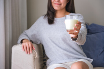 Wall Mural - Closeup image of a young woman holding and showing a glass of fresh milk