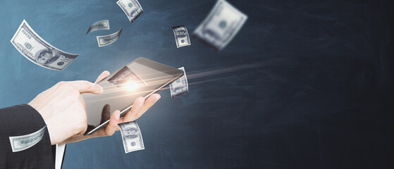 Poster - Close up of male hand using tablet with blurry flying dollar bills on chalkboard background with mock up place. Finance, success and casino concept.