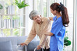 © Bangkok Click Studio - Asian young professional successful friendly female nurse in blue hospital uniform helping supporting physical therapy senior old pensioner unhealthy injury woman patient walking via four legs walker