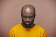 © pressmaster - Portrait of African American man in yellow shirt looking down with sad expression standing on brown background