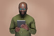© pressmaster - African American man in eyeglasses watching video on digital tablet and smiling standing on brown background