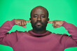 © pressmaster - Portrait of African American man covering his ears from loud noise looking at camera against green background