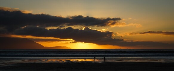 Mesmerizing view of two people on a sandy beach with calm seawater during the golden hour