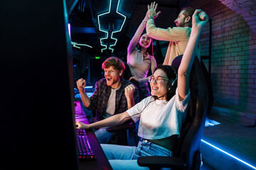 group of friends celebrating victory of asian girl in video game while standing next to her in cyber