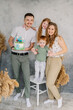 © Serhii - Mom, dad, daughter congratulate son on birthday near grey wall in studio. Happy family holds cake and having fun celebrating a birthday party 2 years. Mother, father hugging kids. Birthday reception.