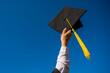 © Михаил Решетников - Close-up of a woman's hand with a graduation cap against the blue sky.
