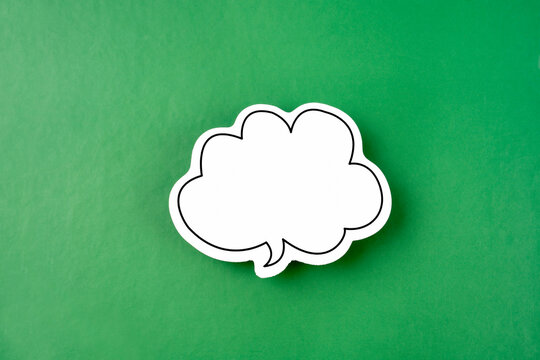 The White speech bubble shaped post it note on green background with copy space.
