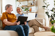 © Westend61 - Happy senior couple sitting with tablet computer on sofa in living room