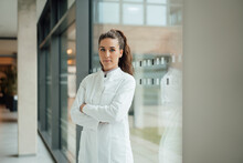 Confident Woman In Lab Coat Standing With Crossed Arms Near Window