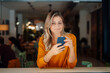 © Westend61 - Smiling woman with bond hair using smart phone in cafe