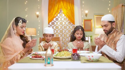 Wall Mural - Indian Muslim family with kids praying at ramadan iftar dinner before eating at home - concept of traditional festival culture, rmzan kareem and family bonding