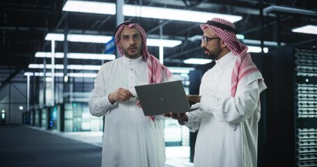 Poster - Middle Eastern Computer Engineer and Cybersecurity Professional Work in Server Room, Talk, Perform System Maintenance Check with Laptop Computer. Specialists Doing Database Diagnostics in Data Center