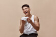 © master1305 - Portrait of handsome young man cheerfully laughing, posing, wiping face after shower against light brown studio background. Concept of male beauty, skincare, cosmetology, men's health