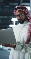 Poster - Vertical Screen: Middle Eastern IT System Engineer Wearing Traditional White Robe, Using Laptop Computer in a Modern Technological Server Farm Facility. Arab Artificial Intelligence Expert at Work