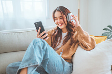 Happy asian woman listening to music from mobile phone while sitting on the the sofa at homes, Smiling girl relaxing with headphones in morning, Time to relax. copy space.