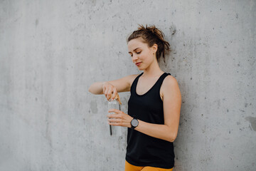 Wall Mural - Young woman drinking water during jogging in city, healthy lifestyle and sport concept.