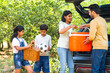 Happy Indian couple with kids taking out bags and picnic bucket from car boot - concept of summer holidays, togetherness and family vacation