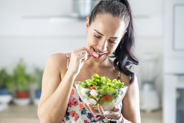 Wall Mural - Healthy lifestyle young woman eating lettuce salad. Young brunette eating healthy food in her kitchen