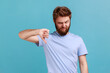 Portrait of bearded man criticizing bad quality with thumbs down displeased grimace, showing dislike gesture, expressing disapproval. Indoor studio shot isolated on blue background.
