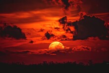 Red Sun With Clouds Behind On The Dark Sky, A Red Sun With Clouds In The Background