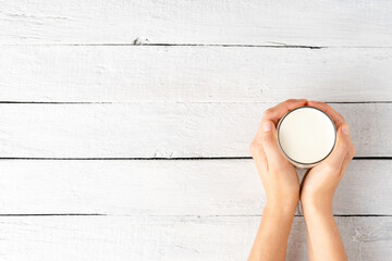 Woman’s hands holding glass of milk on white wooden table with copyspace. Top view