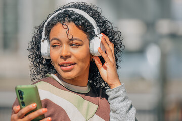 Wall Mural - latin girl with afro hair with headphones and mobile phone in the street