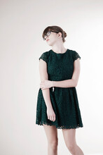 Portrait Of Young Woman Wearing Green, Lace Dress And Horn-rimmed Eyeglasses, Distracted And Looking Upward, Studio Shot On White Background